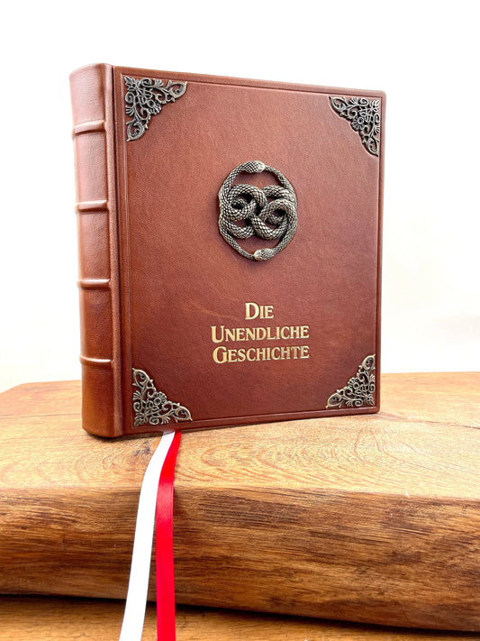  Lederausgabe der Unendlichen Geschichte in braunem Leder mit Zierecken, inspiriert vom Buch im Film. Vorderansicht mit detailreichem, großen AURYN-Emblem in der Mitte und goldener Titelprägung.