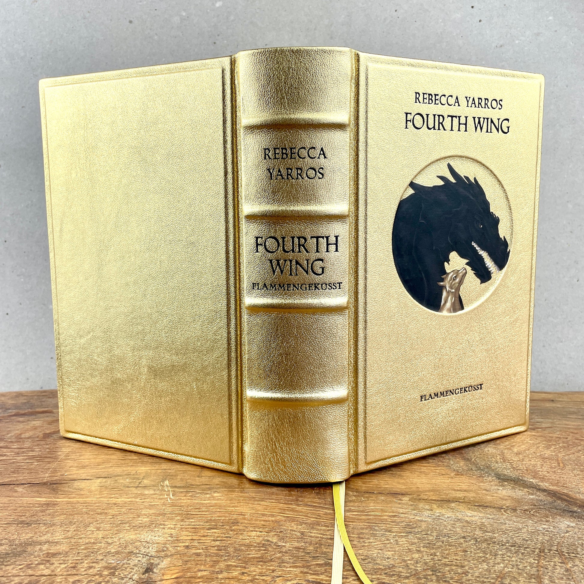 Ledereinband von "Fourth Wing - Flammengeküsst" von Rebecca Yarros, in goldenem Leder mit vertiefter Drachenillustration und schwarzen Titelprägungen.